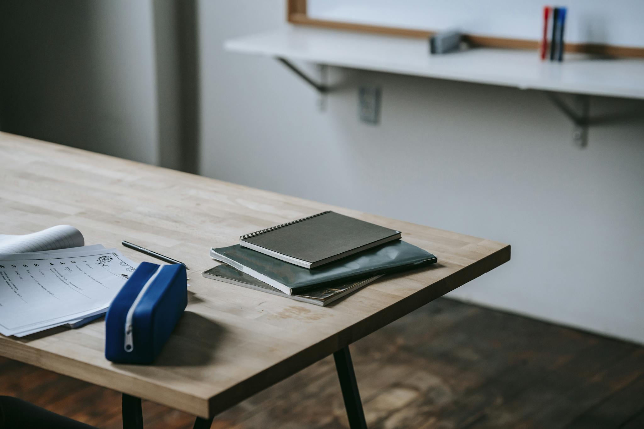 A neatly organized classroom desk with notebooks, papers, and pen case in a modern educational setting.