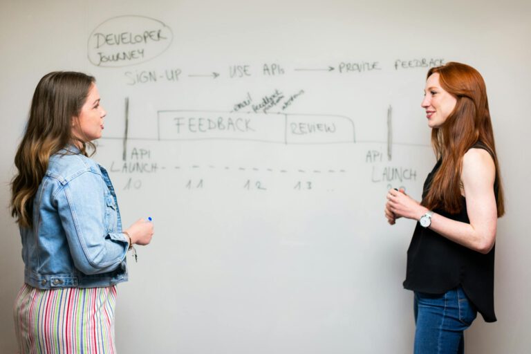 Two women engaging in a discussion about API development processes at a whiteboard.