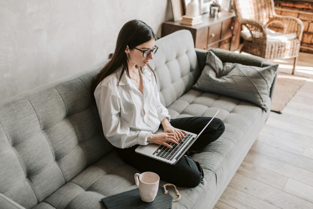 Woman in a cozy home setting working on a laptop for remote work and relaxation.